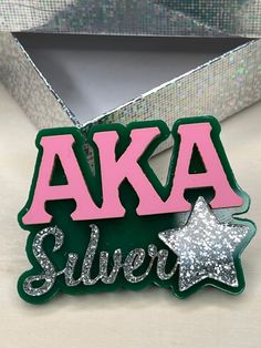 a pink and green aka silver pin sitting in front of a tinsel box