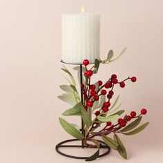 a white candle with red berries and green leaves on a black metal stand against a pink background