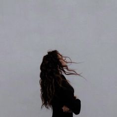 a woman standing in front of a white wall with her hair blowing in the wind