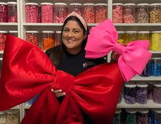 a woman holding two large pink bows in front of shelves with many different colored sprinkles