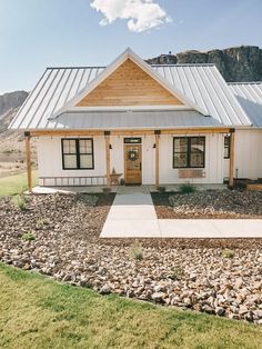 a white house with a metal roof in the middle of some grass and rocks on the ground