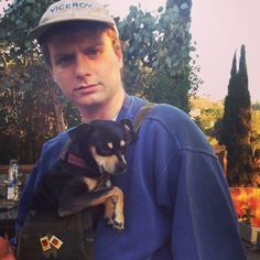 a man holding a small dog in his arms while wearing a hat and vest with patches on it