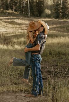 a man and woman in cowboy hats hugging each other while standing on a dirt road