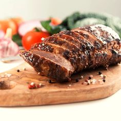 meat on a cutting board with vegetables and seasoning in the backgroung