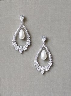 a pair of white pearl and crystal earrings on a gray surface with pearls in the middle