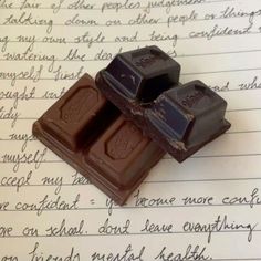 two pieces of chocolate sitting on top of a piece of paper with writing in the background