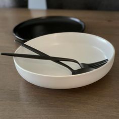 two black and white plates with forks in them sitting on a wooden table next to each other