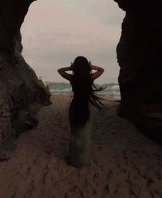 a woman standing in front of a cave on the beach