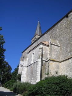 an old stone church with a steeple against a blue sky and green bushes on the side