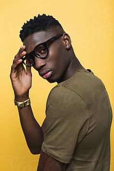 a young man wearing glasses and a t - shirt against a yellow background by jodi lenski for stocksy photography