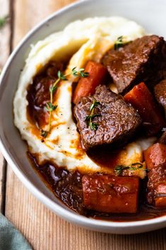 a white bowl filled with meat and mashed potatoes on top of a wooden table