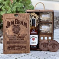 a bottle of bourbon and coasters in a wooden box on a brick floor next to some plants