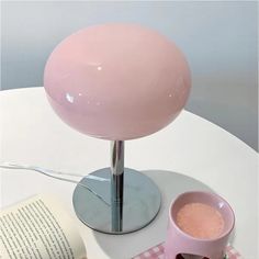 a pink lamp sitting on top of a table next to a coffee cup and book