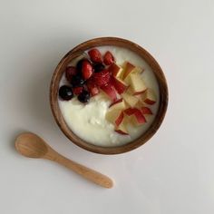 a bowl filled with yogurt and fruit next to a wooden spoon on a white surface