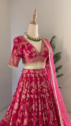 a pink lehenga on display in front of a white mannequin and green plant