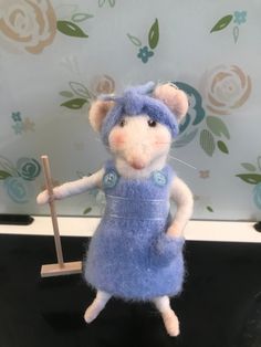 a needle - felt mouse holding a stick in its paws and wearing a blue dress