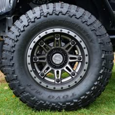 the front wheel and tire of a black four - door jeep parked on green grass