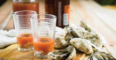 three glasses filled with liquid sitting on top of a wooden table next to oysters