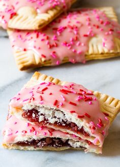 three pastries with pink icing and sprinkles on them sitting on a table