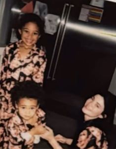 two women and a child are sitting in front of a refrigerator