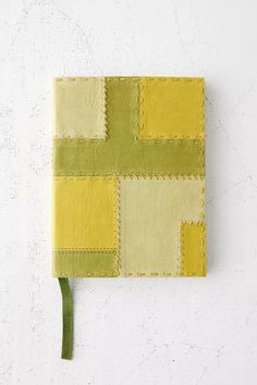 a yellow and green patchwork notebook on a white surface with a plant in the corner