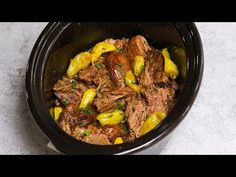 a black bowl filled with meat and vegetables on top of a white countertop next to a spoon