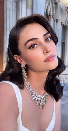 a woman wearing a white dress and some necklaces on her neck is posing for the camera