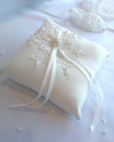 a white ring pillow on top of a bed covered in pearls and satin ribbons with a bow