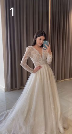 a woman in a wedding dress taking a selfie with her cell phone while standing next to a curtain