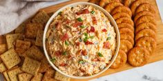 a bowl of dip surrounded by crackers on a cutting board