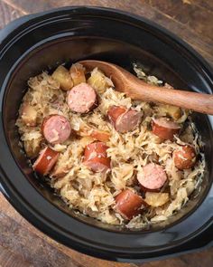 a crock pot filled with sausage and rice on top of a wooden table next to a spoon