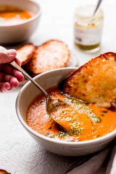 a bowl of soup with bread on the side and someone holding a spoon in it