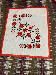 a quilted table runner with red and green flowers on it, sitting on a bed