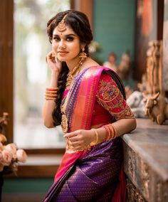 a woman in a pink and purple sari sitting on a ledge with her hand near her face