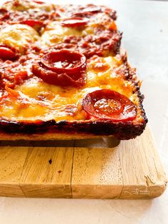 a square pizza with pepperoni and cheese on a cutting board