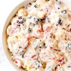 a white bowl filled with fruit salad on top of a marble countertop next to a fork