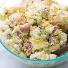 a glass bowl filled with potato salad on top of a white countertop next to a wooden spoon