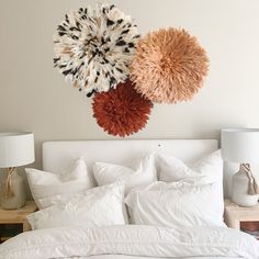 a white bed topped with lots of pillows next to a wall mounted art piece on the wall