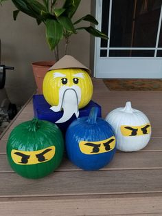 three pumpkins with faces painted on them sitting on a wooden table next to a potted plant