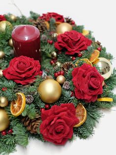 a christmas wreath with red roses, oranges and a candle on the center surrounded by pine cones