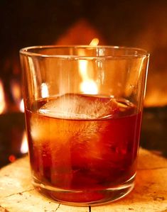 a glass filled with liquid sitting on top of a wooden table next to a fire place