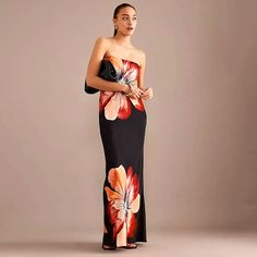 a woman in a black and red dress with flowers on the side, standing against a gray background