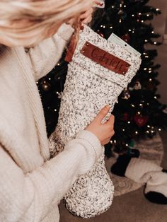 a woman holding a christmas stocking in front of a christmas tree with the word merry written on it