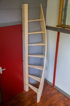 a curved wooden shelf next to a red door in a room with wood flooring