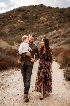 a man and woman walking down a dirt road with a baby in their arms while holding an infant