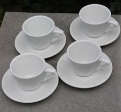 four white cups and saucers sitting on top of a cement tableclothed surface