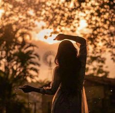 a woman standing in front of a tree at sunset