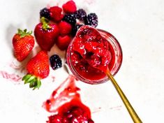 strawberries and raspberry sauce in a jar on a white surface with gold spoon