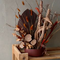 an arrangement of dried flowers in a vase on a wooden table with a decorative fan