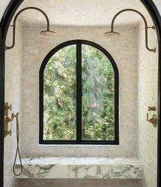 an arched window in a white bathroom with marble counter tops and floor to ceiling windows